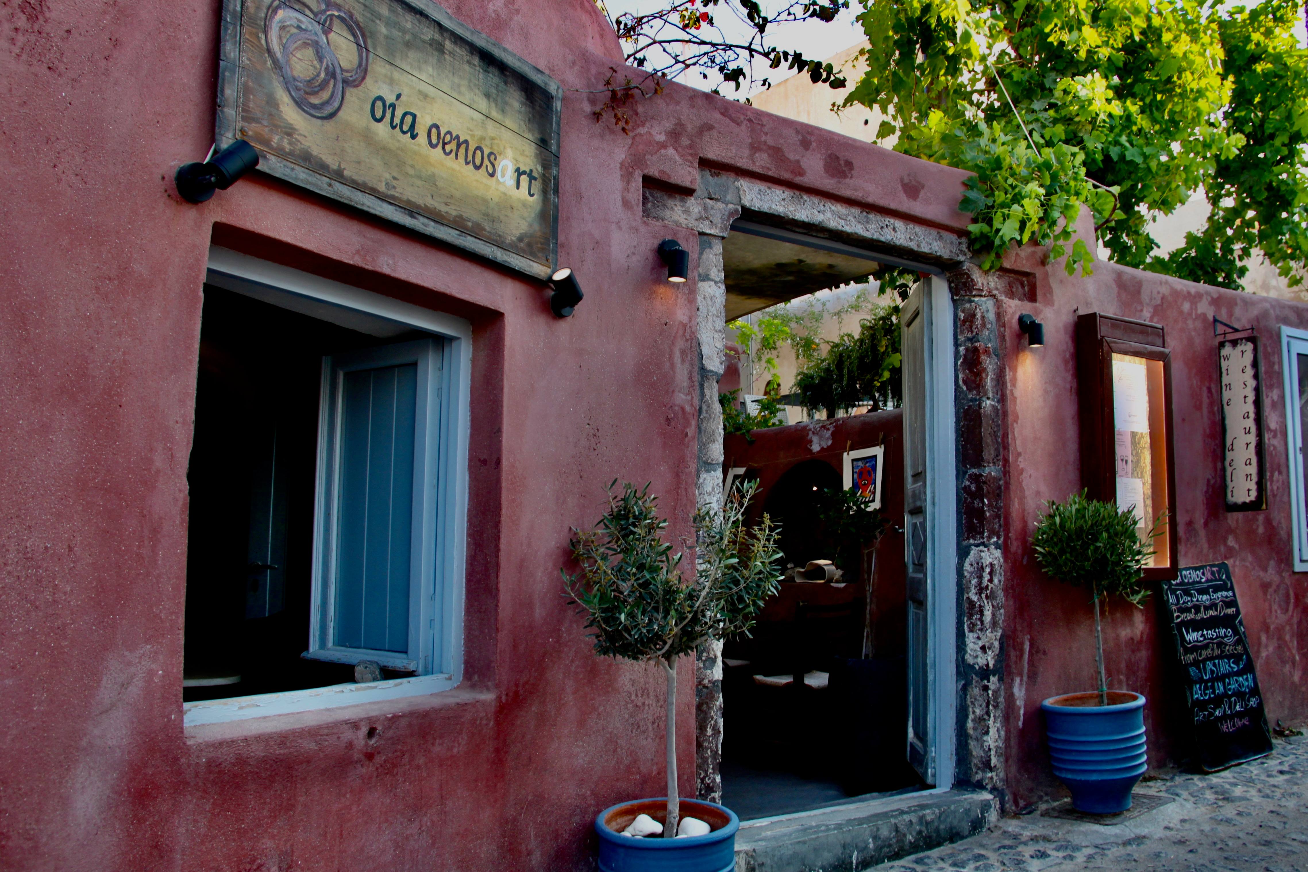 Rose-coloured entrance of Oia Oenosart beneath green vines in Oia